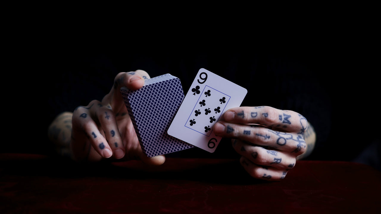 Hand with tattooed fingers holding two playing cards against a dark background